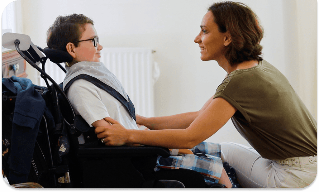 Souris d'enfant en fauteuil roulant avec une femme souriante en interaction chaleureuse.